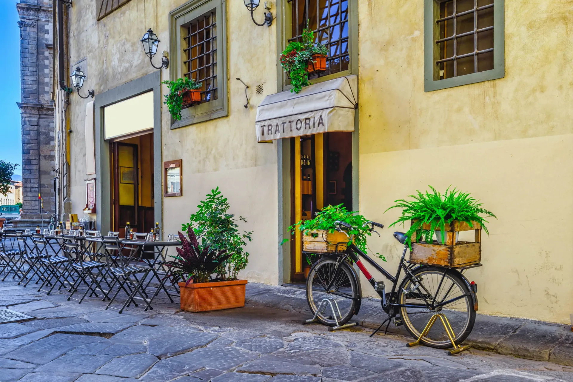 Trattoria med udendørs caféborde og cykel med blomster