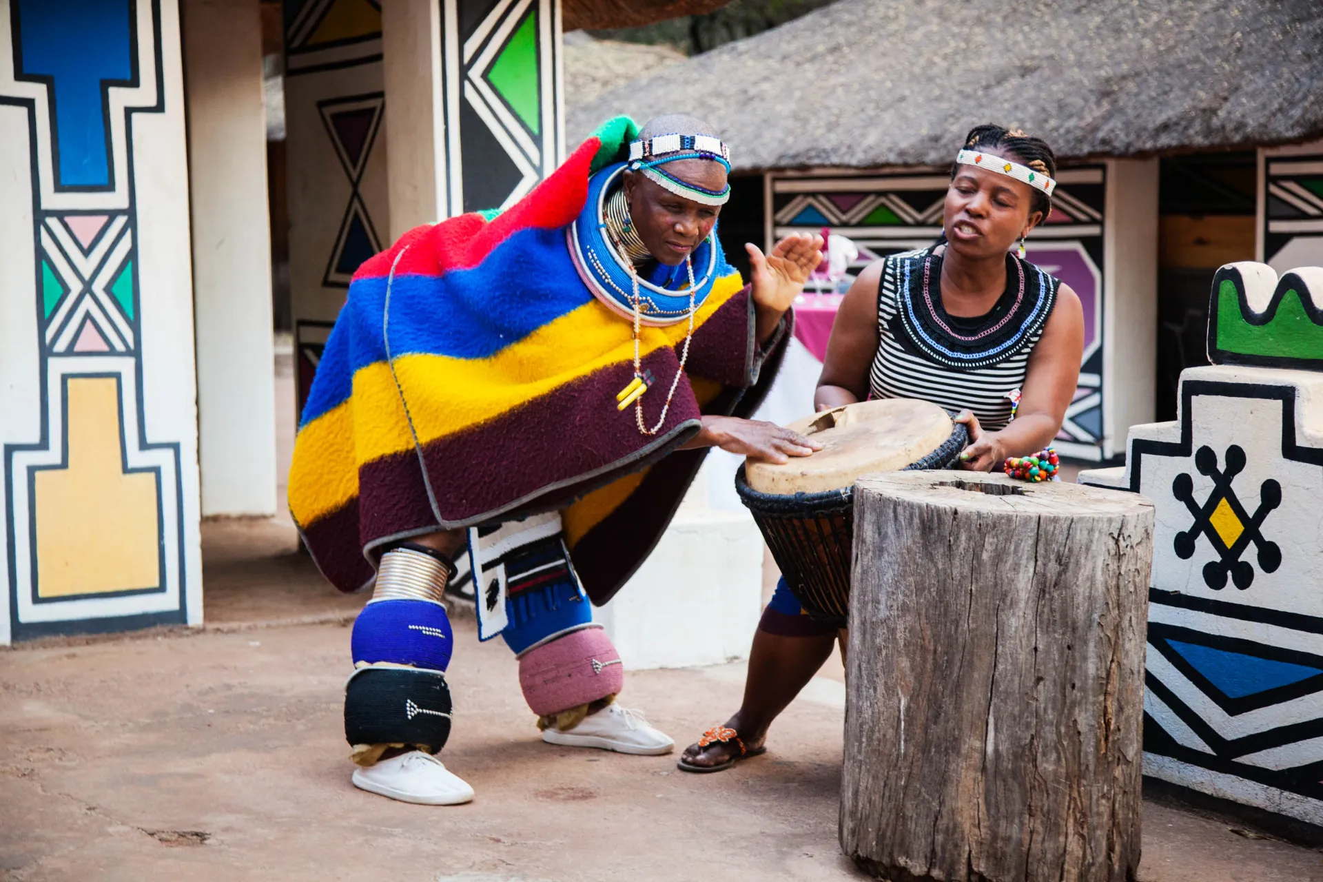 Ndebele-kvinder i farverige traditionelle klæder danser og spiller tromme i en historisk landsby ved Pretoria Ndebele-kvinder i farverige traditionelle klæder danser og spiller tromme i en historisk landsby ved Pretoria
