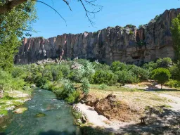 Flod i den frodige Ihlara-dal med stejle klippevægge i baggrunden under blå himmel
