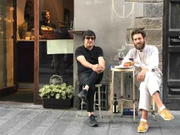 To mænd nyder et glas vin ved et lille bord på gaden