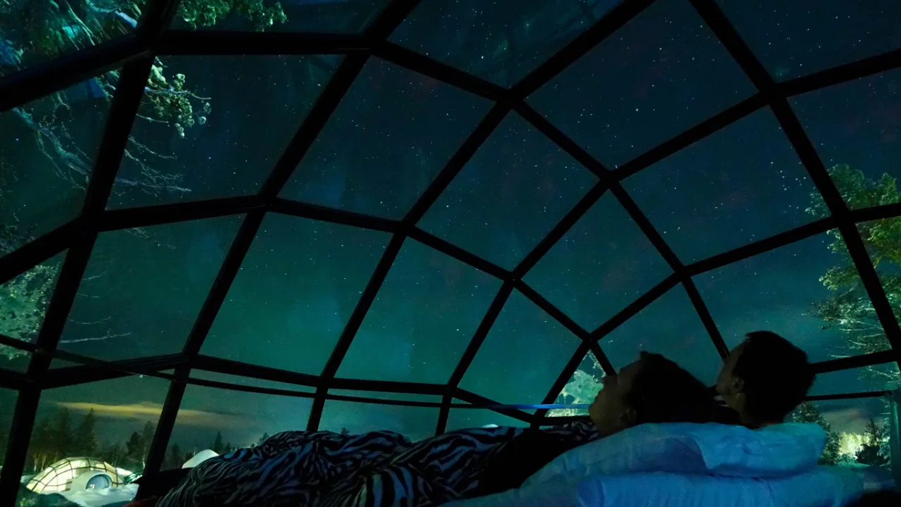Nordlys betragtes fra sengen på et glasiglo-hotel