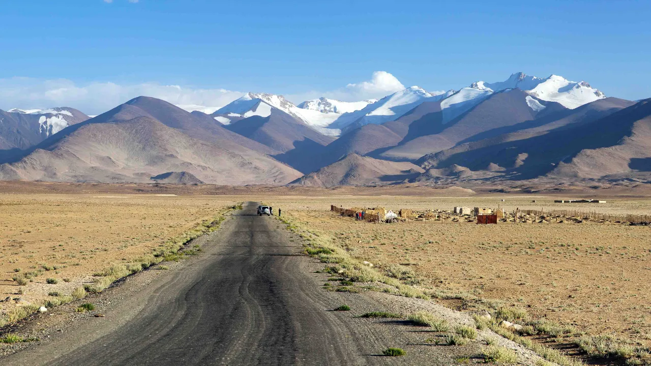 En øde og barsk strækning langs den berømte Pamir Highway med Tadsjikistans sneklædte bjergtinder i baggrunden En øde og barsk strækning langs den berømte Pamir Highway med Tadsjikistans sneklædte bjergtinder i baggrunden
