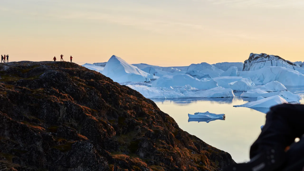 Udsigt over isbjerge ved Sermermiut nær Ilulissat med vandrere på klipperne Udsigt over isbjerge ved Sermermiut nær Ilulissat med vandrere på klipperne