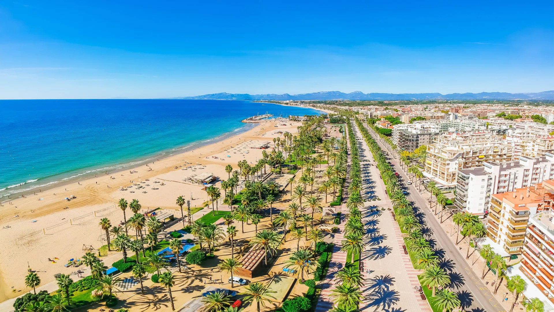 Hoteller, palmer, strand, turkisblåt hav, solskin og bjerge i baggrunden Hoteller, palmer, strand, turkisblåt hav, solskin og bjerge i baggrunden